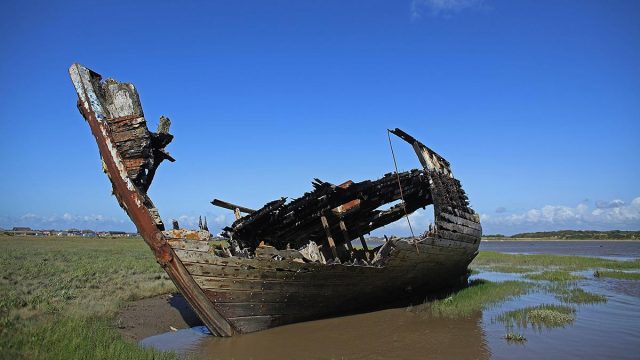 The rotting hulk of an old boat decaying in the sands of Fleetwood Marshes in England.