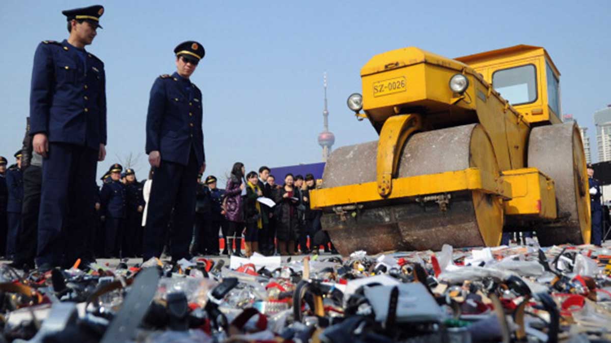 Local policemen and members of the public look on as the road roller crushes the counterfeit products in Shanghai.