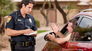 A law enforcement officer with a ticket book stands by the side of a vehicle he has stopped, as the motorist pleads his case and trys to explain why he shouldn't receive a citation or moving violation.