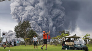 People play golf as an ash plume rises in the distance from the Kilauea volcano on Hawaii's Big Island on May 15, 2018 in Hawaii Volcanoes National Park, Hawaii