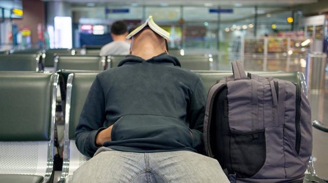 A man waiting in an airport terminal with a book covering his face. Pic: Getty