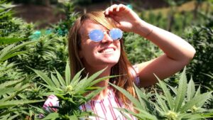 A smiling young woman standing amid cannabis plants. Pic: Getty