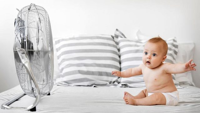 Baby boy sitting in front of electric fan feeling the air on his face. Pic: Getty
